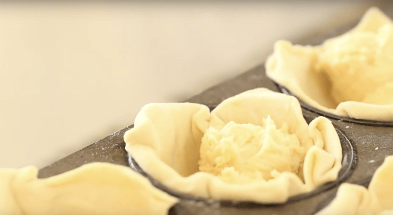Filling puff pastry shells in a muffin tin with almond filling