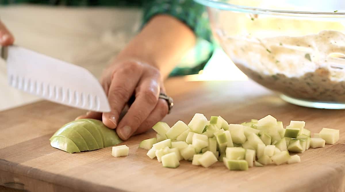 A person chopping green apples on a cutting board