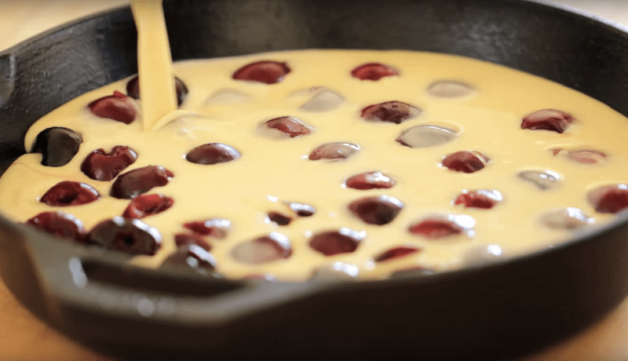 batter being poured on top of cherries in a cast iron skillet
