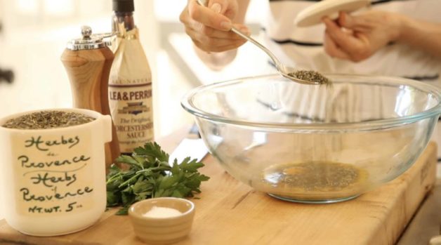 A person holding a spoon sprinkling herbs de Provence spices into a clear bowl 