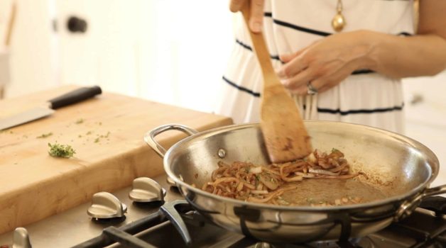 onions being caramelized in a stainless steel pan with a wooden spatula 