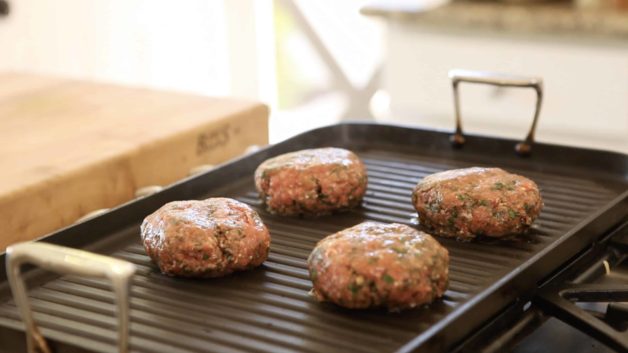 burger patties being grilled on a grill pan over a gas stove