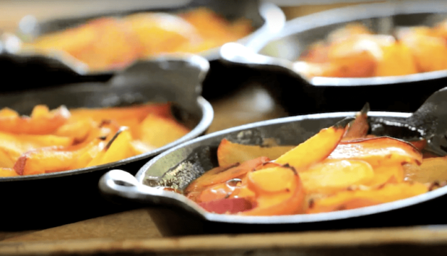 cooked peaches in mini cast iron baking dishes on a sheet pan