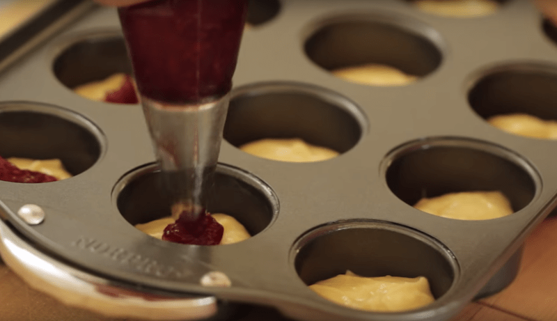 raspberry jam being piped into batter of raspberry almond thimble cakes