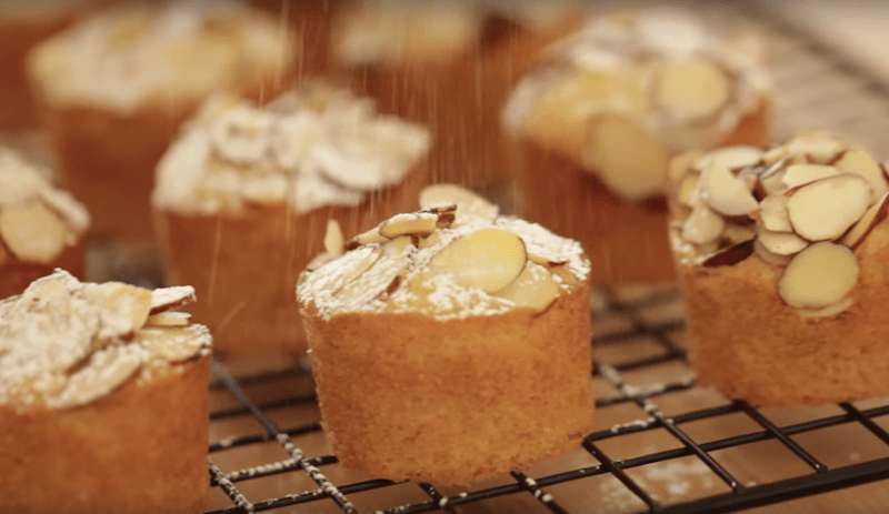 powdered sugar being sprinkled on top of raspberry almond thimble cakes