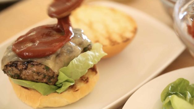 adding smoked ketchup on a cheeseburger served on a white plate