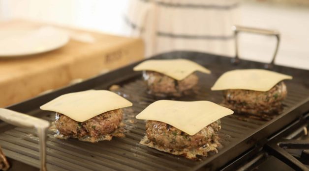 Swiss cheese being melted on burger patties on a grill 