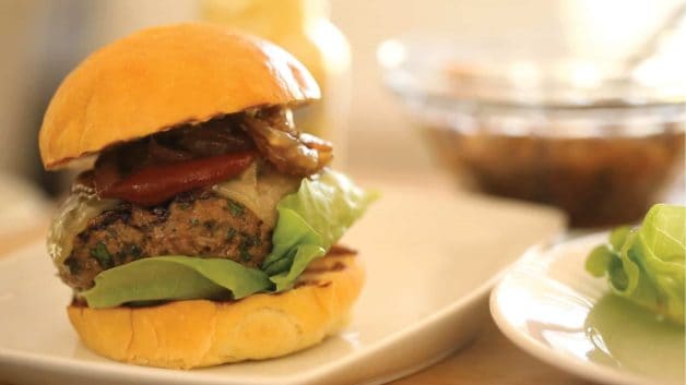 burger served on a white plate with bibb lettuce to the side and a bowl in the background