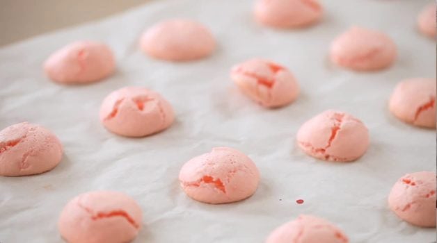 Cracked macaron shells on a baking tray with parchment paper