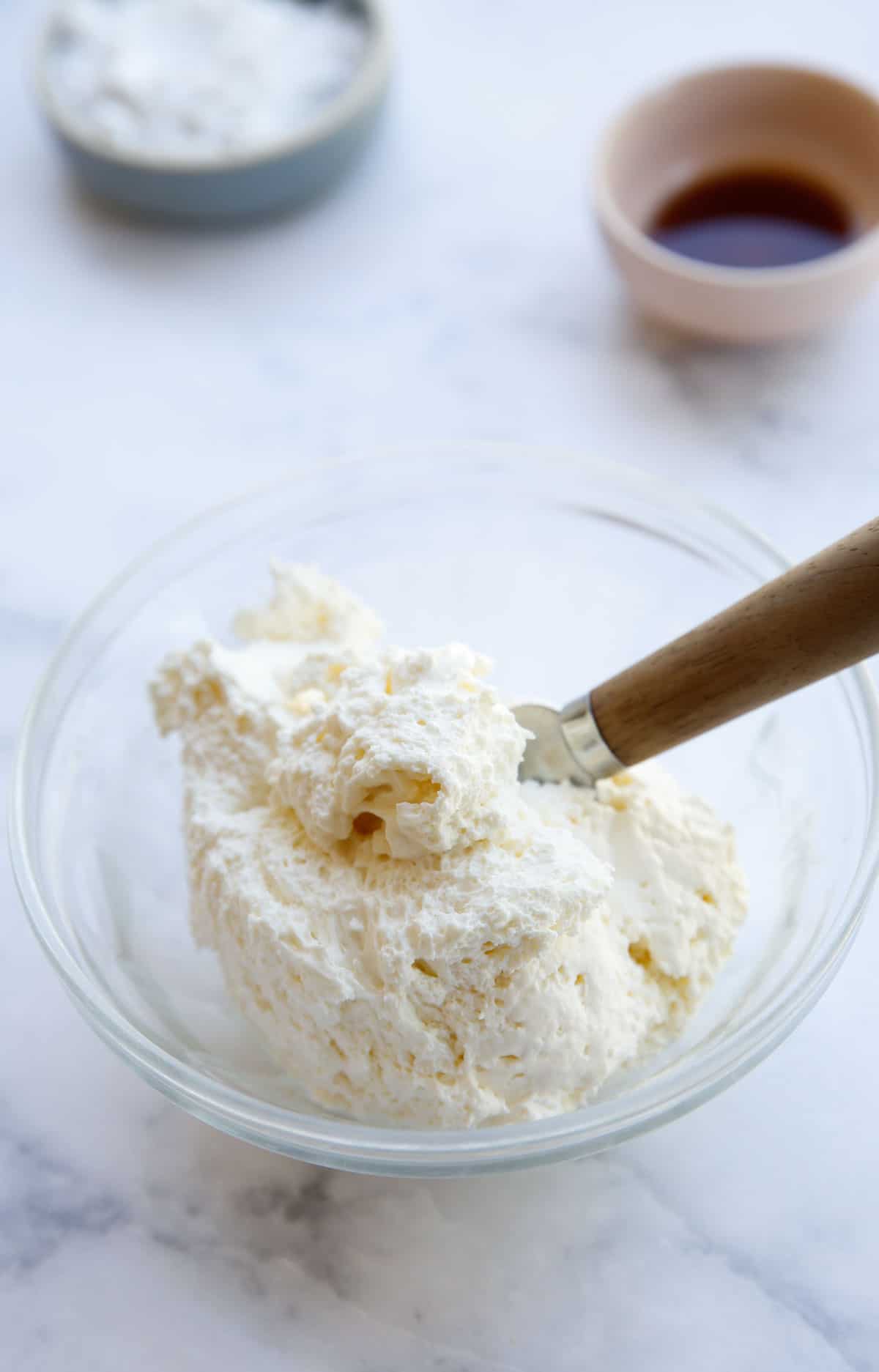 a bowl of whipped cream cheese with a small bowl of powdered sugar and vanilla in the background