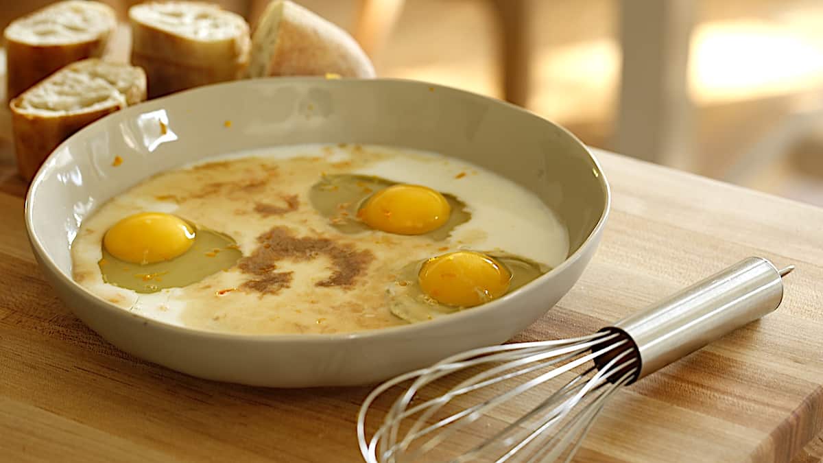 shallow bowl with eggs, milk, vanilla and sugar with whisk in foreground