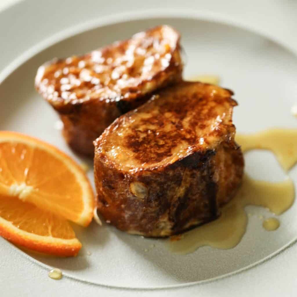 Two Slices of Pain Perdu on a plate with sliced oranges.