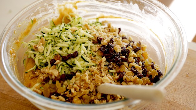 A bowl of food on zucchini bread batter with fruits, nuts and grated zucchini