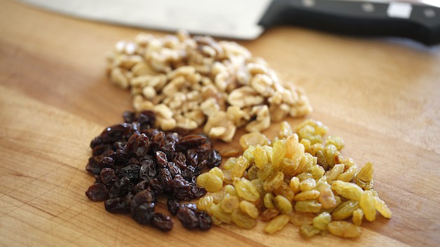 a cutting board with a grouping of raisins, yellow raisins and chopped walnuts