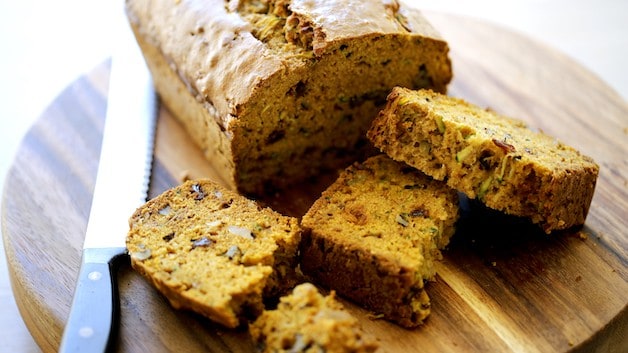 A piece of zucchini bread on a cutting board with full loaf in background