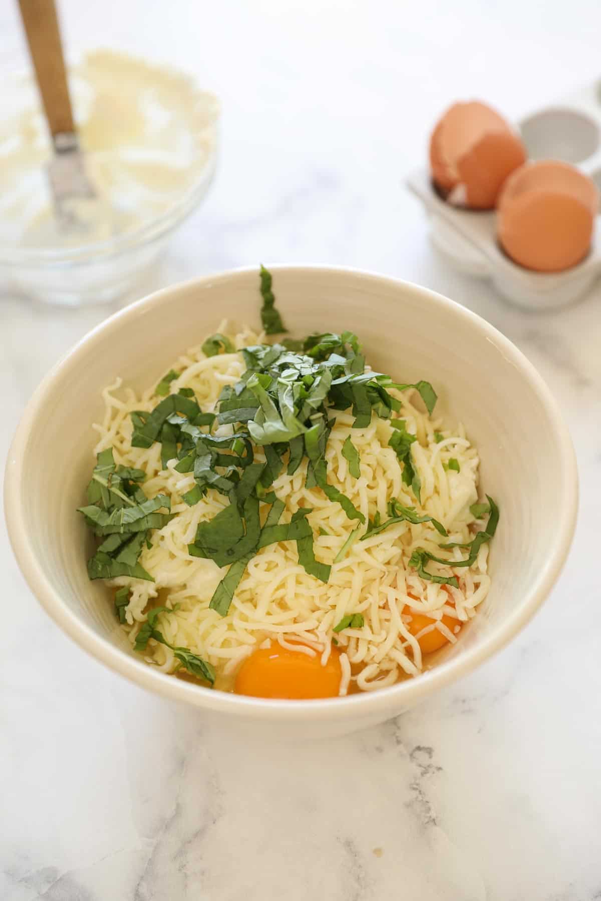 a bowl of ricotta cheese with eggs, basil and mozzarella cheese