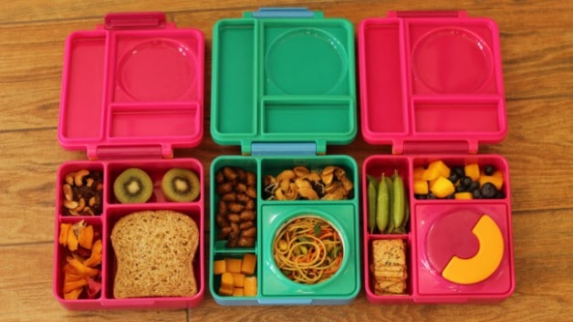three Pink and green omie lunchboxes open and filled with food