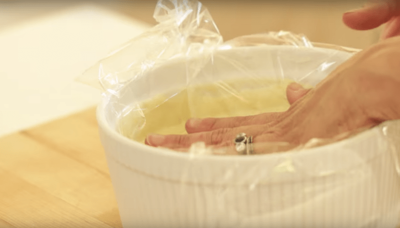 plastic wrap being pressed up against the custard mixture in a large white bowl 