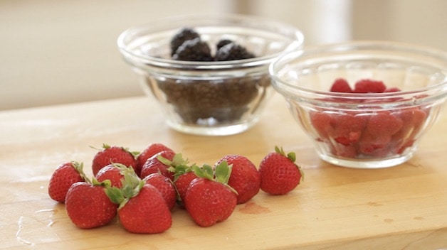 strawberries on a cutting board and blackberries an raspberries in clear bowls