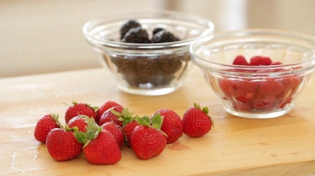 strawberries on a cutting board and blackberries an raspberries in clear bowls