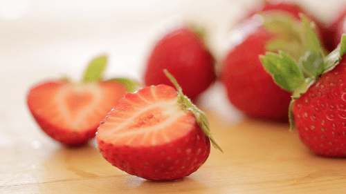 fresh cut strawberry on a wood board with more strawberries in the background 