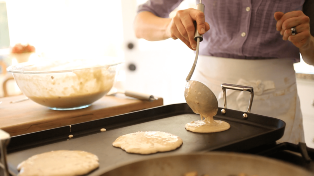 pancakes batter being ladled on to a hot griddle to cook 