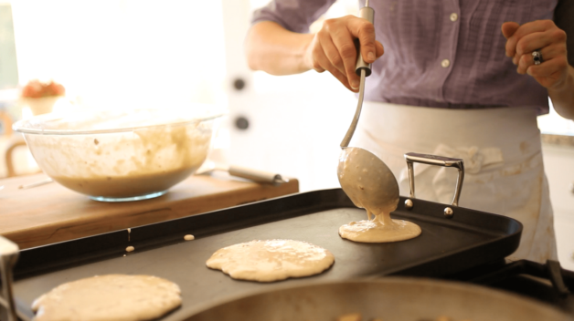 pancakes batter being ladled on a hot griddle to cook 