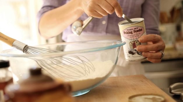 a person with a measuring spoon inside a can of baking powder measuring quanity