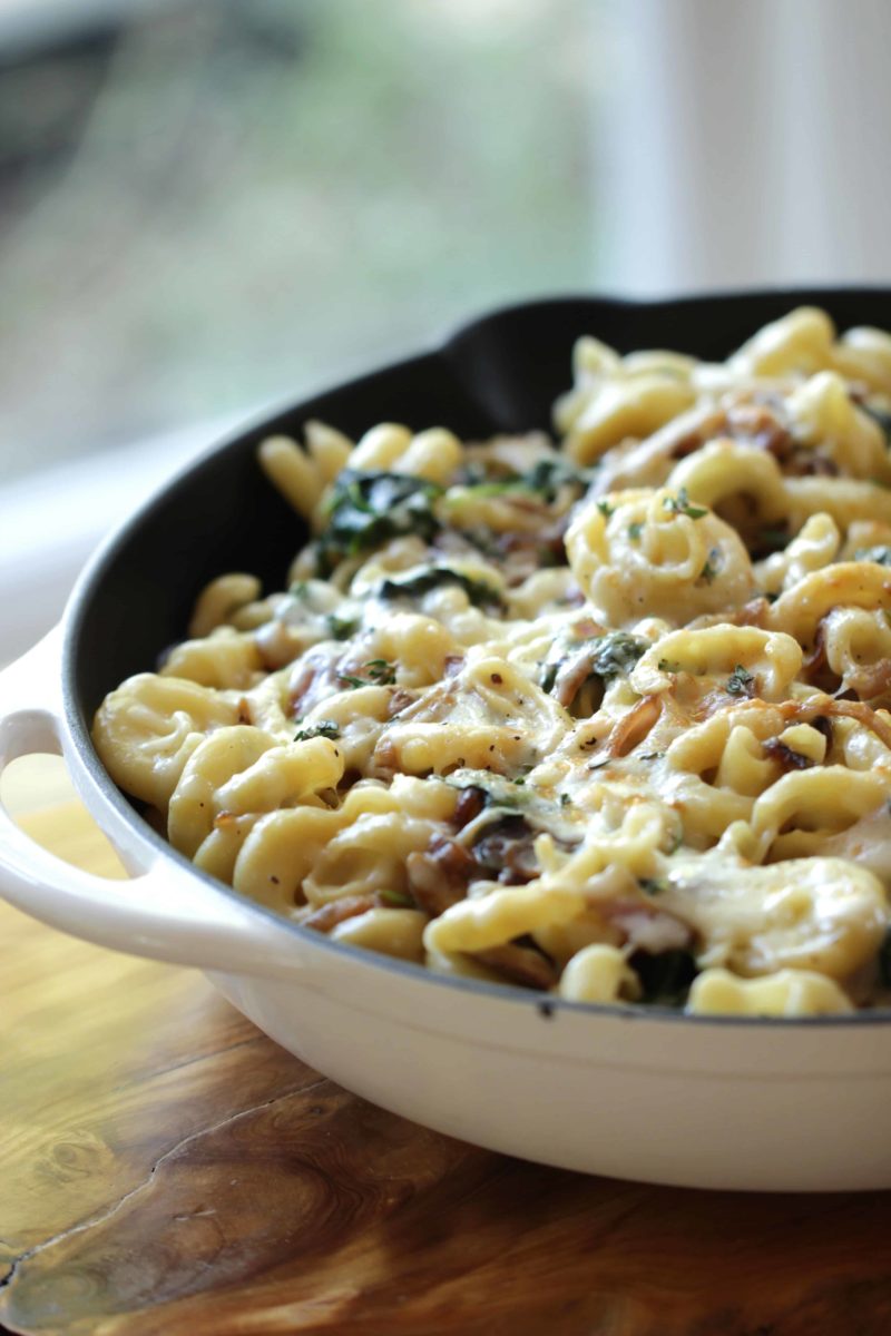 A large white skillet filled with cheesy pasta with vegetables