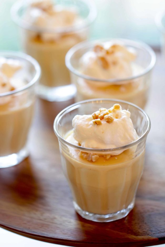 Salted Caramel Puddings served with fresh whipped cream in little glass jars on a wood surface