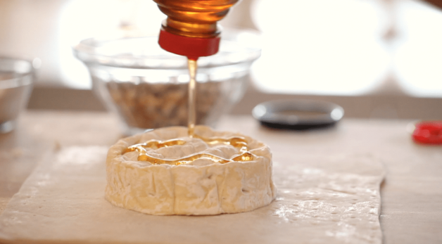 honey drizzled on top of a brie wheel fon a cutting board