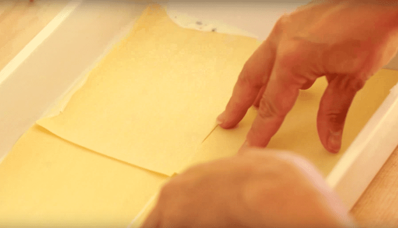 lasagna noodle being placed in a lasagna pan