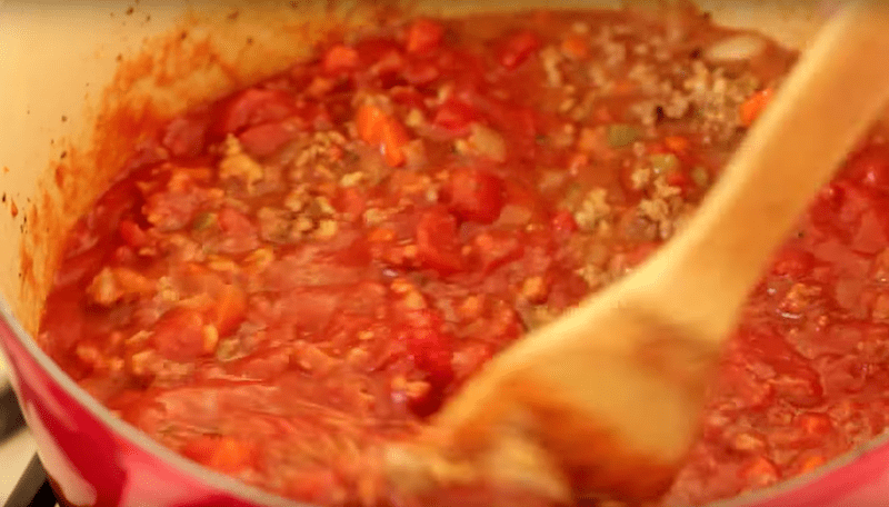 meat sauce in a large pot being mixed with a wooden spoon