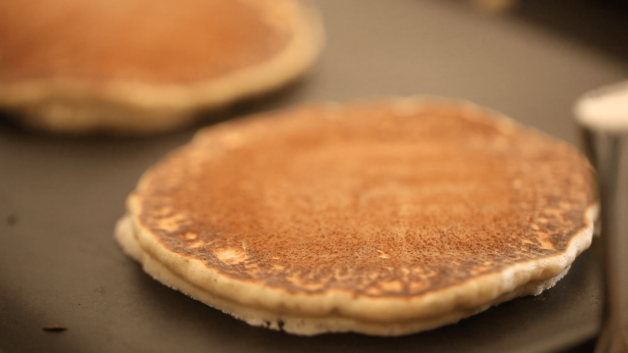 Pancakes being cooked to golden brown on a black griddle