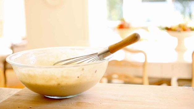 pancake batter in a clear mixing bowl with whisk on a wood counter
