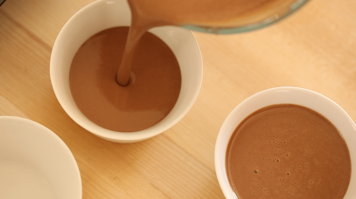 Pouring chocolate custard into white ramekins 