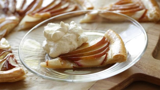 A slice of an Easy Pear Tart on a glass plate with whipped cream 