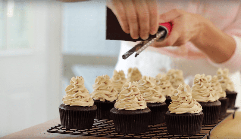 chocolate is grated on top of frosted cupcakes 