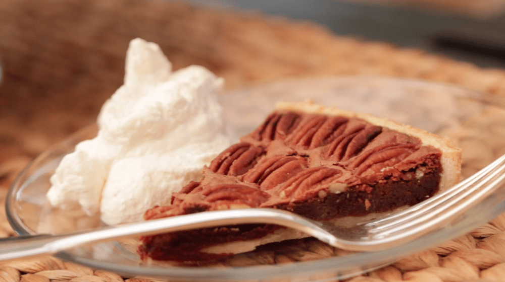 Chocolate Pecan Tart sliced and put on a clear plate with a dollop of whipped cream and a fork