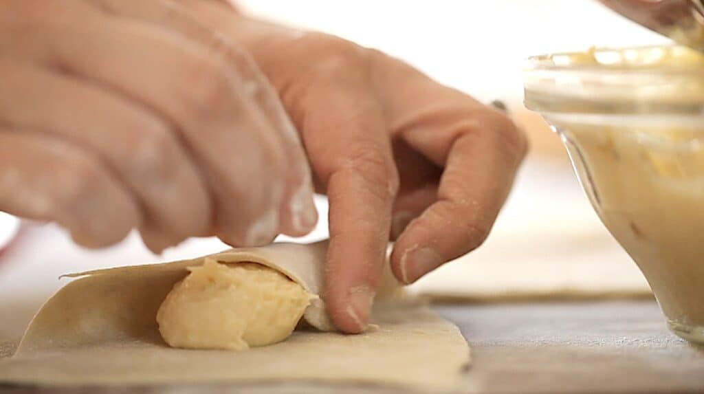 a person folding over a corner of puff pastry over almond filling
