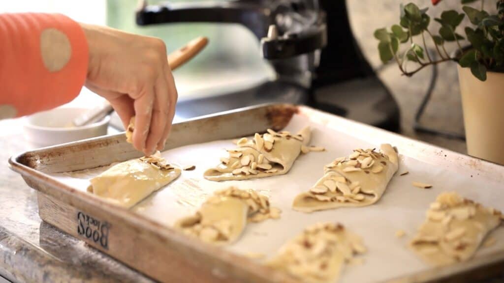 placing raw almonds on top of croissants reading for the oven 