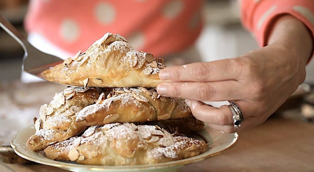 A person placing a freshly baked croissant on a platter