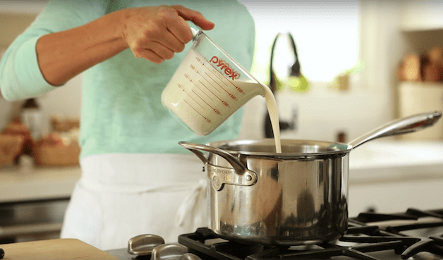 cream being poured into a large pot over a stove for a Cranberry Panna Cotta Recipe