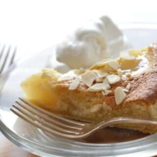 Pear Almond Tart Recipe served with some whipped cream on a white plate with a silver fork