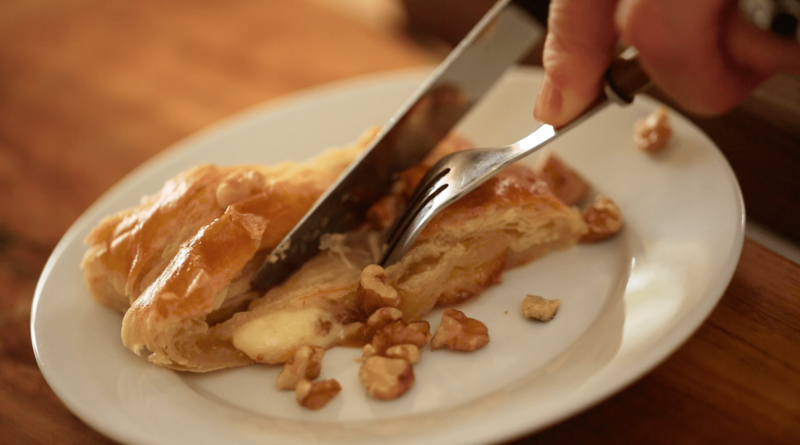 Cutting into a slice of a fig and Brie Braid with a fork and a knife