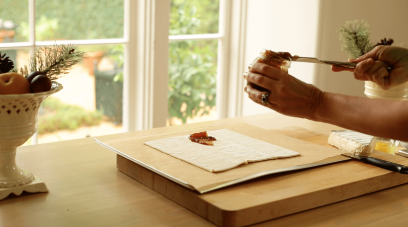 A person spreading fig jam on a sheet of puffed pastry on a baking sheet