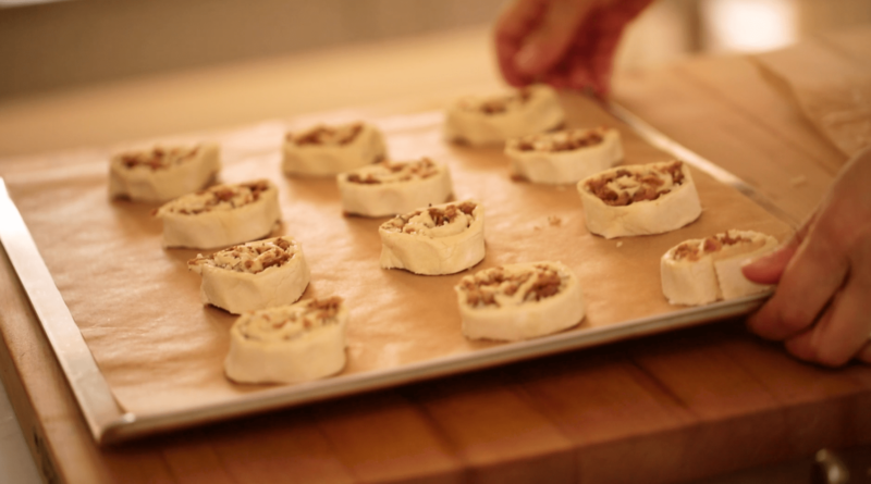 A person holding a baking sheet with sliced pinwheels filled with sausage and cheese 