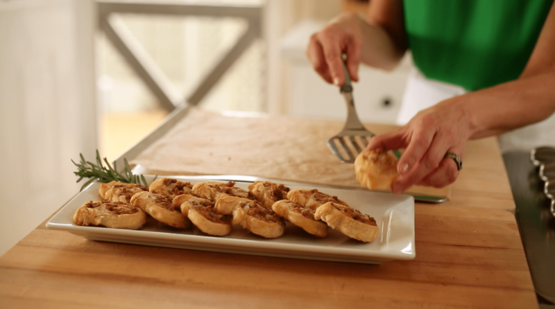 A person placing Sausage and Cheese Pinwheels on a rectangular Platter