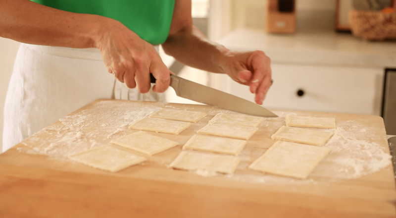 A person cutting puff pastry into small rectangles on a floured cutting board