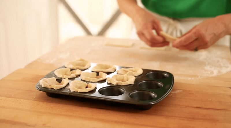 a person filling a mini muffin tin with puff pastry